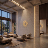 A modern lobby with large windows, neutral armchairs and sofas around low tables, a beige rug, and Notredame LED Small Wall Lights in gold casting geometric patterns on the light textured walls.