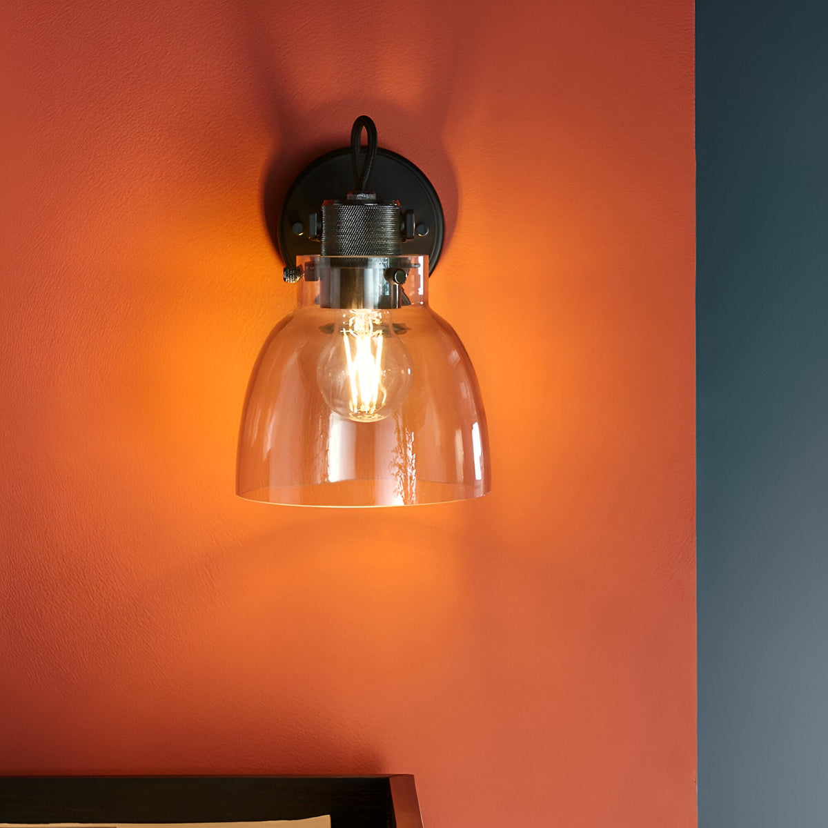 Camden Wall Light in black and chrome with clear glass dome shade and exposed bulb, mounted on a burnt orange wall.