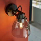 Camden Wall Light in black chrome finish with knurled detail, braided cable, and clear glass dome shade over an exposed bulb, mounted on an orange wall.