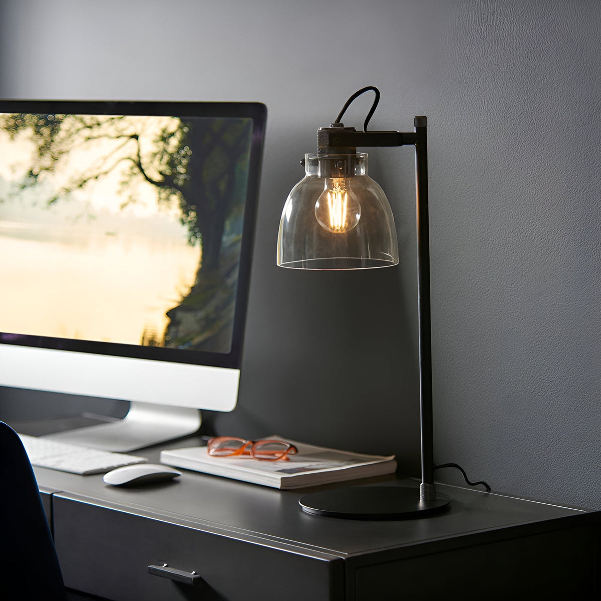 Endon Camden industrial task table lamp in matt black with knurled details and smoked glass shade, on a desk beside a monitor, keyboard and glasses.