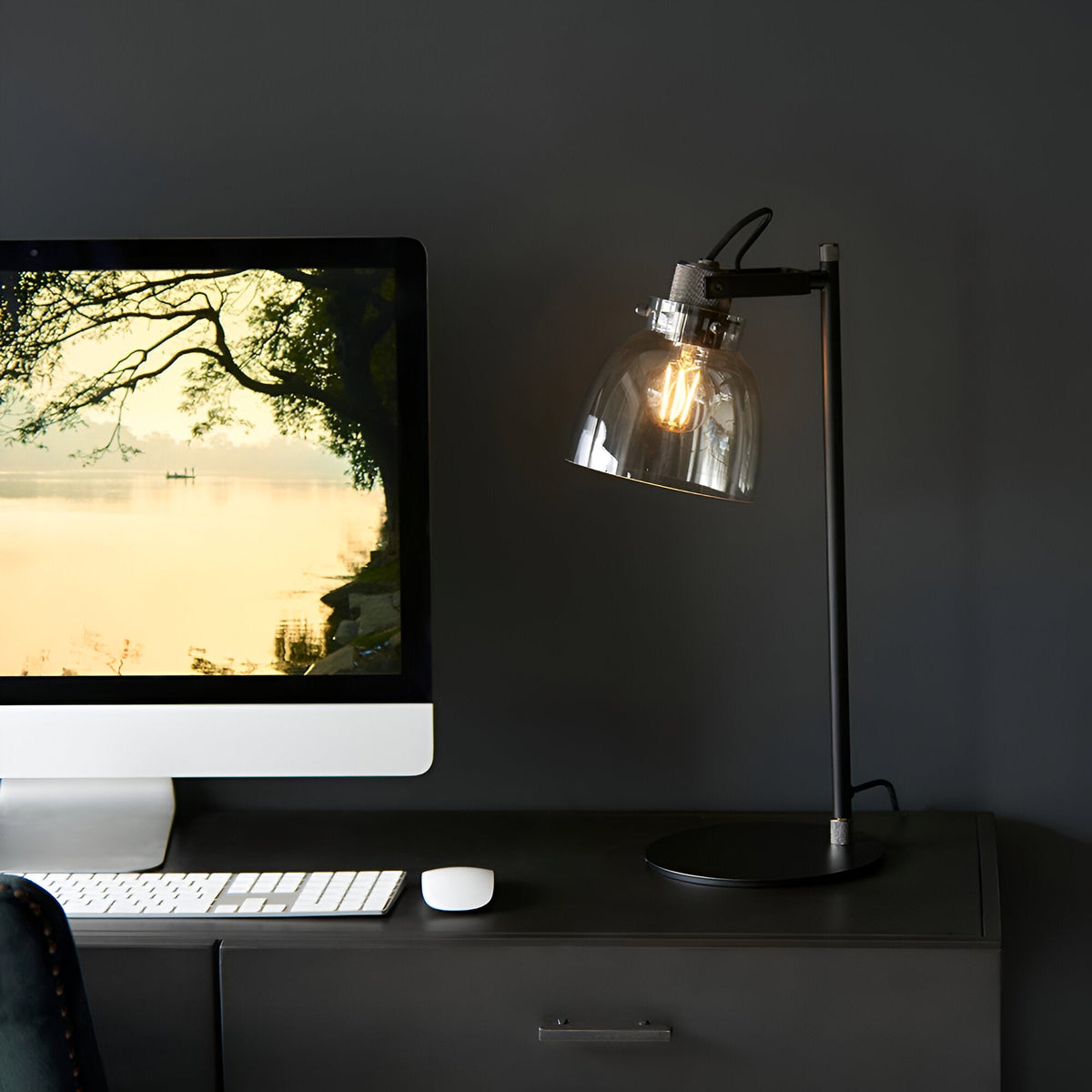 Endon Camden industrial task table lamp in matt black with smoked grey glass shade and filament bulb, lit on a desk beside a monitor and keyboard.