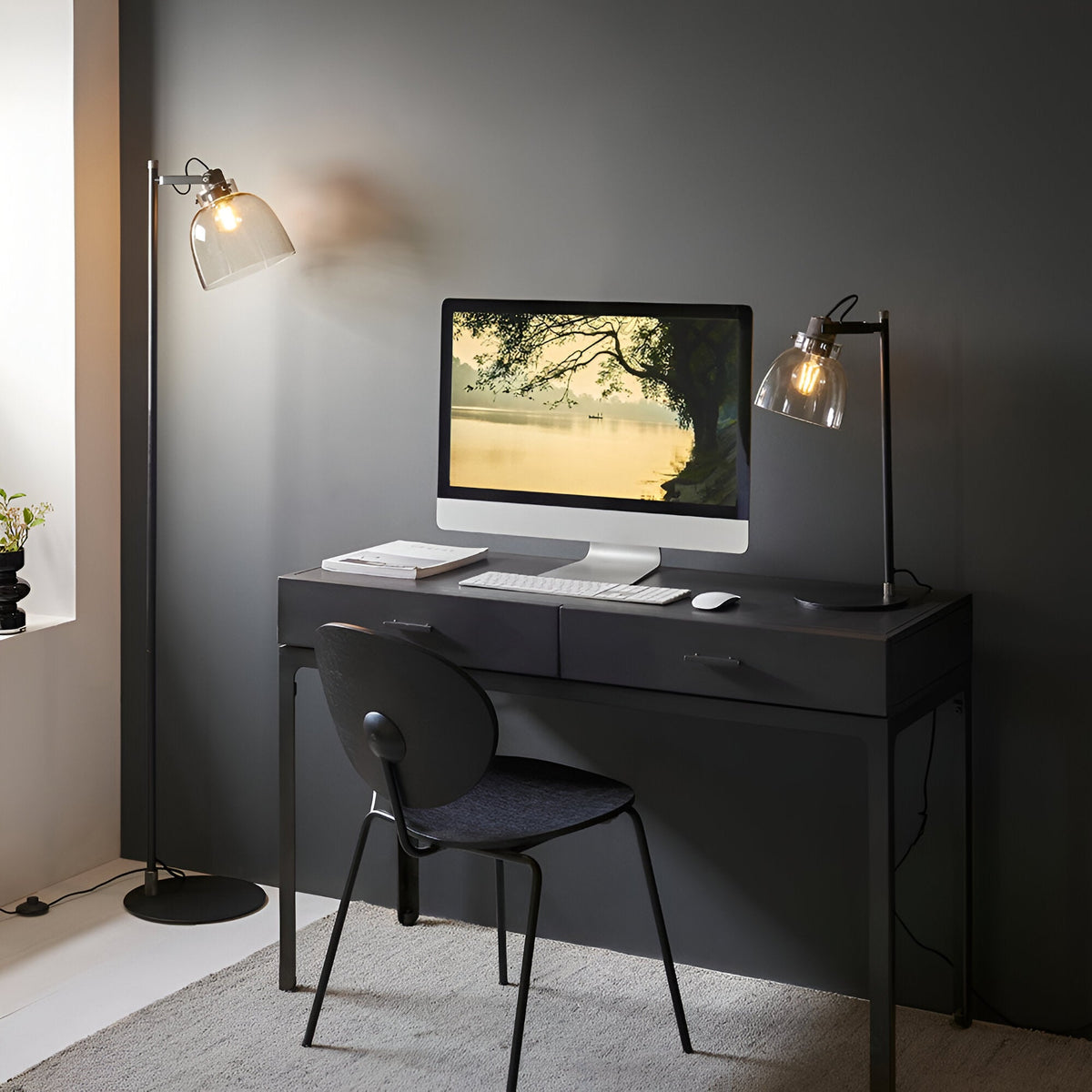 Endon Camden industrial task table lamp in matt black with smoked glass shade and adjustable head, on a dark desk beside a monitor and floor lamp.