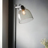 Endon Camden industrial floor lamp in matt black with adjustable head, smoked grey tinted glass shade and filament bulb, against a light grey wall.