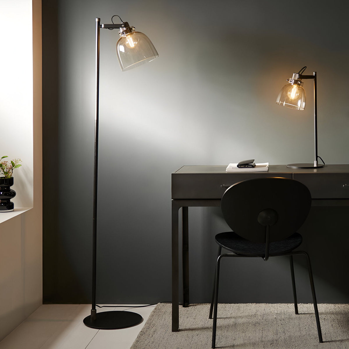 Endon Camden industrial floor lamp in matt black with adjustable head and smoked glass shade, beside a dark desk with matching table lamp and chair.
