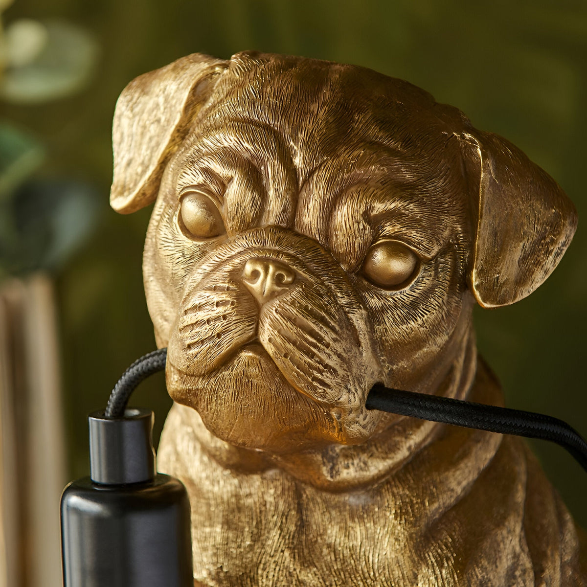 Close-up of the Endon Charthurst table lamp's gold resin pug figure, showing sculpted facial detail beside the black fabric cable and inline switch.