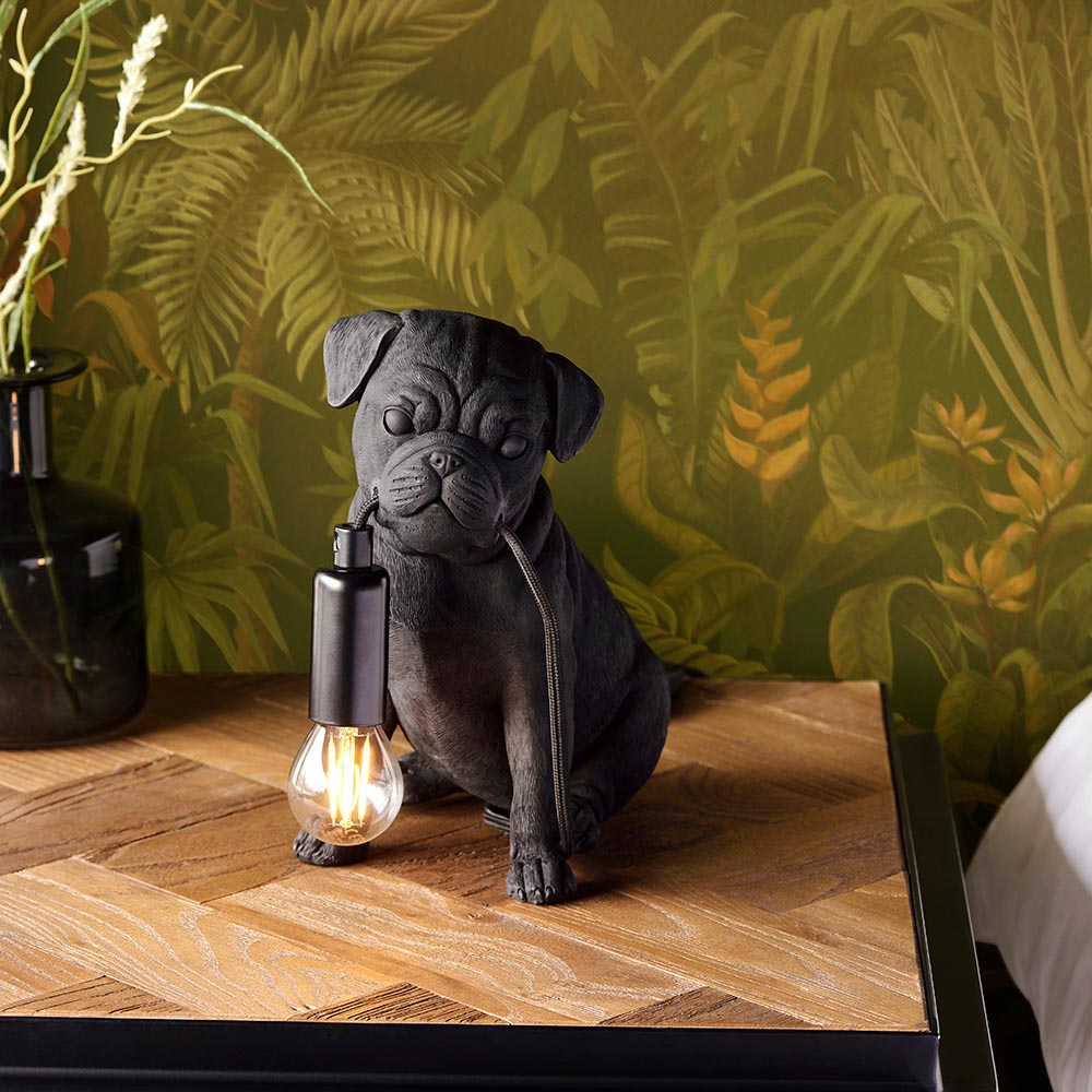 Endon Charthurst matt black resin pug table lamp holding an E14 filament bulb, on a wooden bedside table against tropical leaf wallpaper.