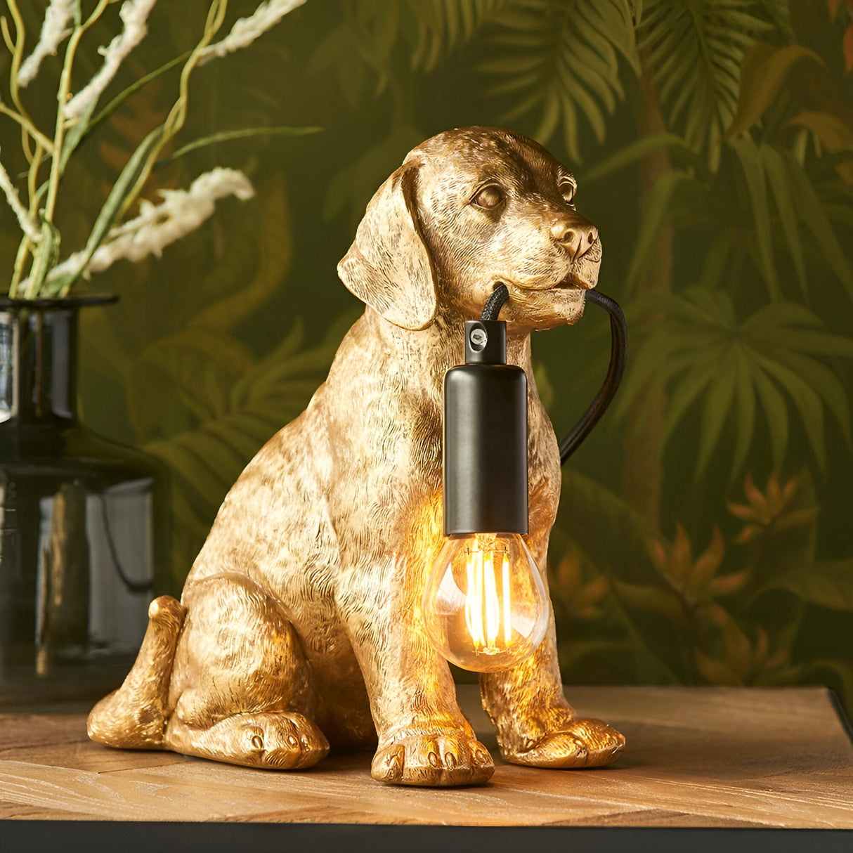 Brockworth Table Lamp in gold resin Labrador puppy shape holding a black lamp holder with exposed filament bulb, displayed on a wooden surface.