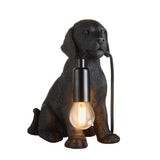 Endon Brockworth table lamp shaped as a matt black resin Labrador puppy holding an E14 filament bulb by a black cable, on a plain white background.