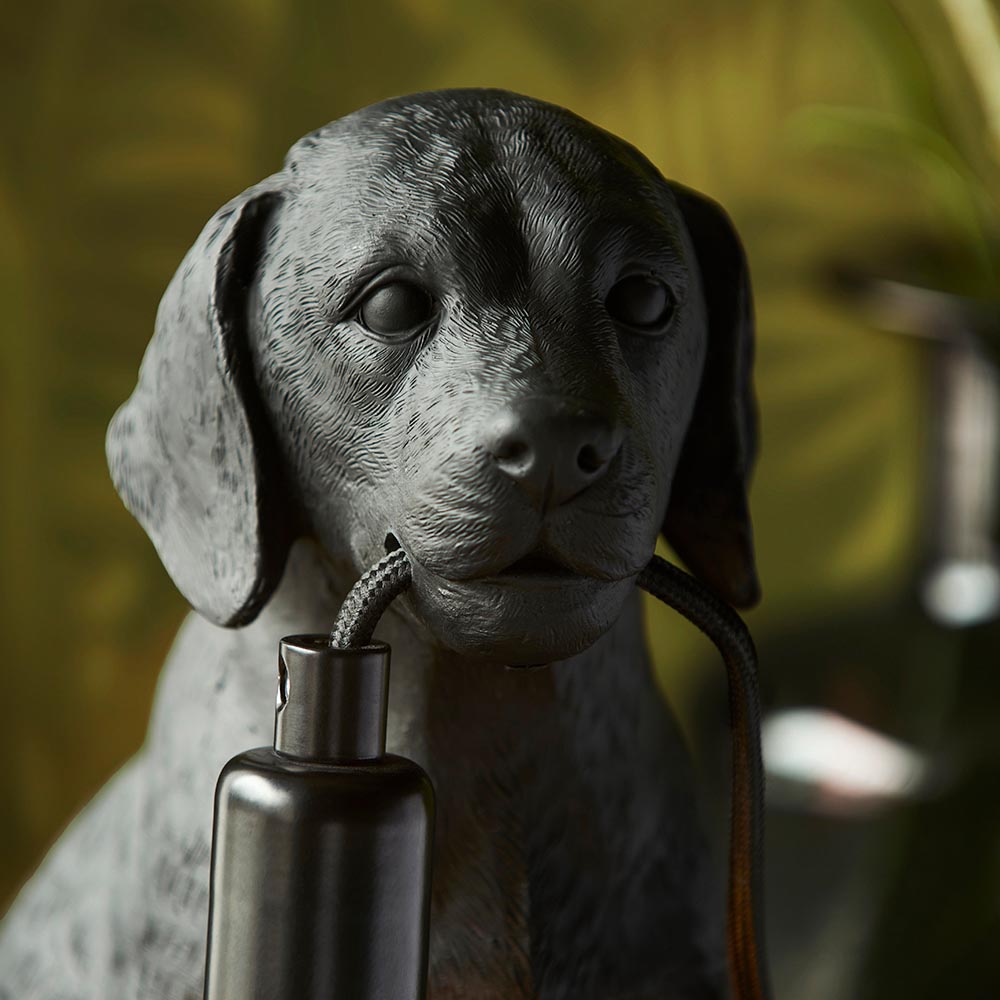 Endon Brockworth matt black table lamp shaped as a resin Labrador puppy, holding an E14 bulb holder on a black cable against a leafy backdrop.