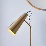 Endon Brockleigh table lamp with adjustable antique brass conical shade and black fabric flex, shown beside a round gold-framed mirror on a pale background.