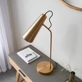 Endon Brockleigh antique brass table lamp with adjustable conical shade and E27 fitting on a grey desk beside a book, styled in a bedroom setting.
