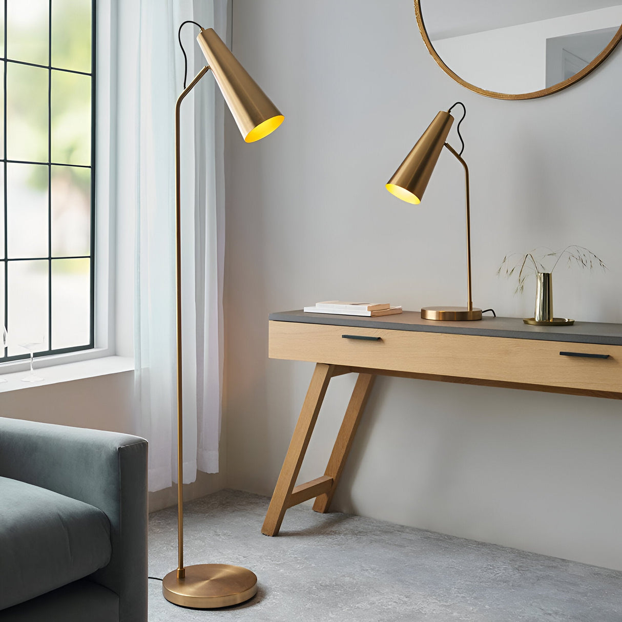 Endon Brockleigh antique brass table lamp with adjustable conical shade on a wooden console, beside a matching floor lamp by a window in a living room.