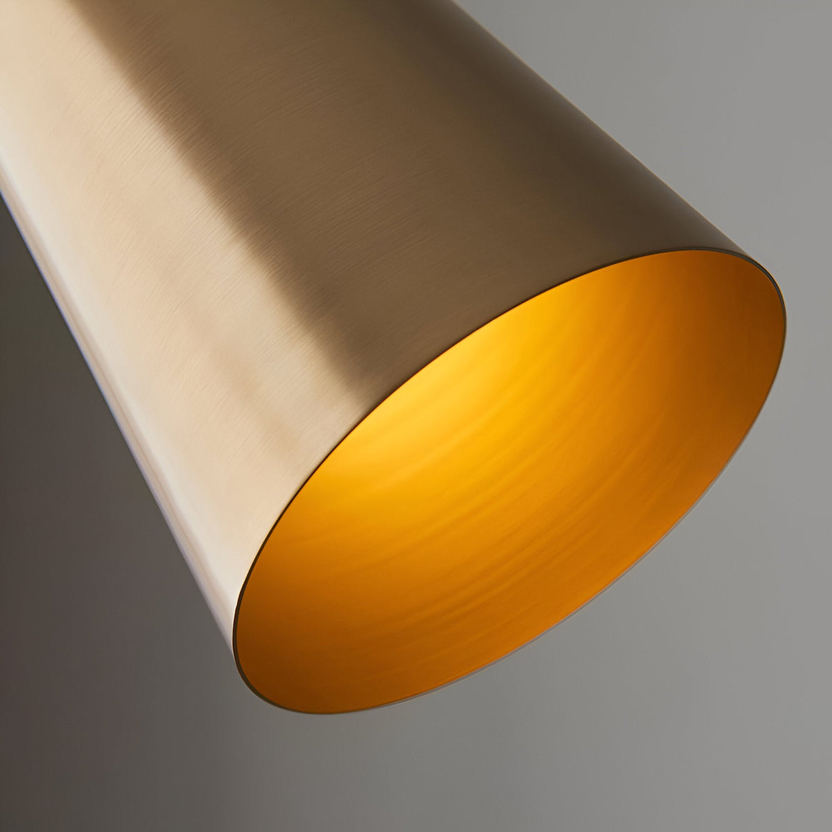 Close-up of the Brockleigh Task Floor Lamp's cylindrical antique brass shade, showing the brushed metal finish and glowing interior against a grey background.
