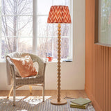 Endon Ashwood floor lamp with stacked bamboo sphere base in natural wood and pleated orange patterned shade, beside a wicker chair by a sunlit window.