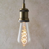 Endon 4W E27 LED filament twist bulb with clear teardrop glass and spiral filament, lit in warm white, suspended from an antique brass pendant holder.