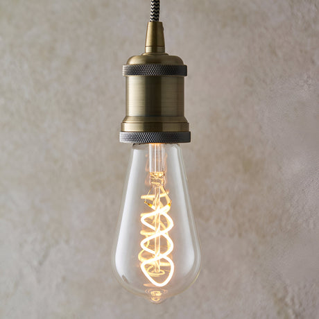 Endon 4W E27 LED filament twist bulb with clear teardrop glass and spiral filament, lit in warm white, suspended from an antique brass pendant holder.