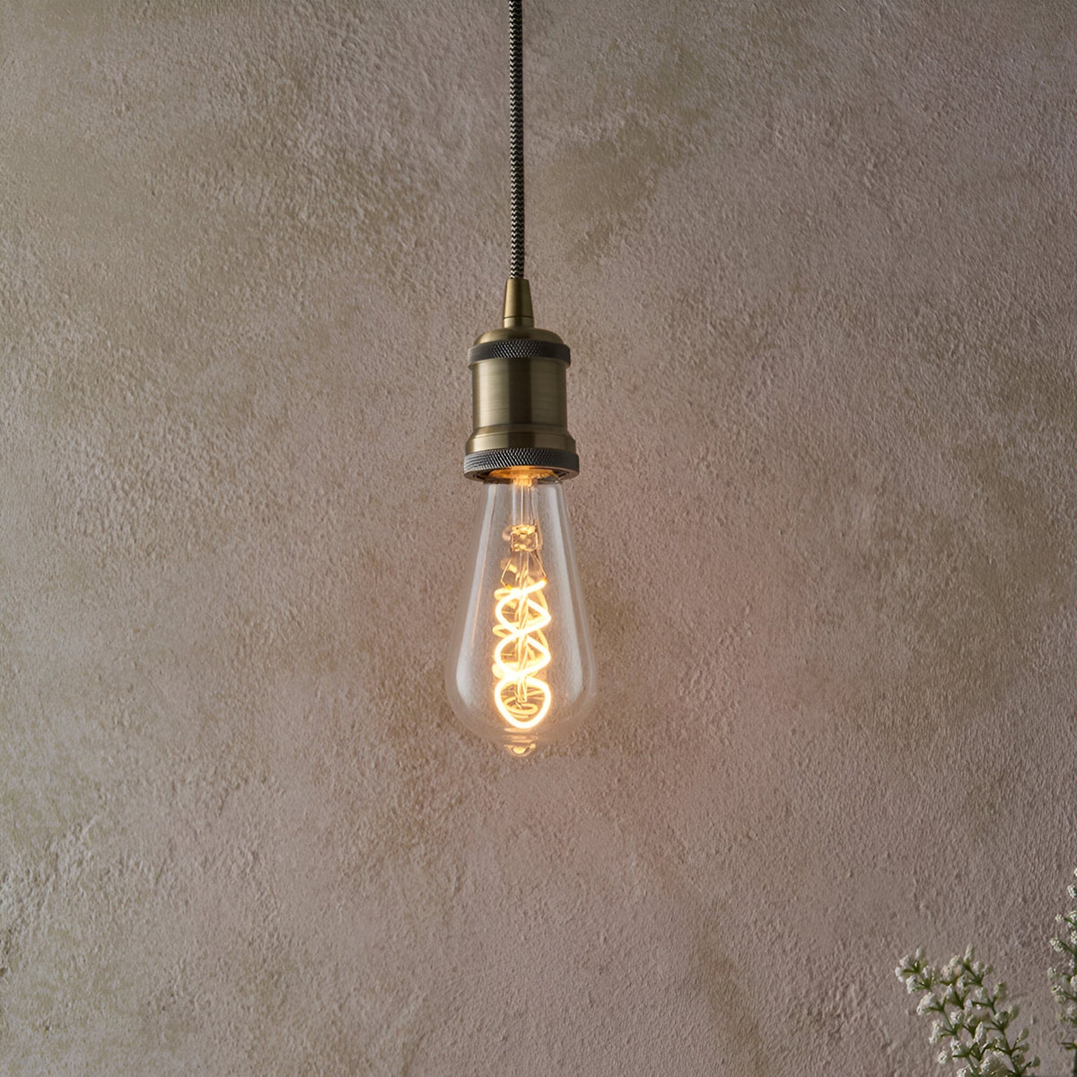 Endon 4W E27 LED filament twist bulb with clear pear-shaped glass and warm amber spiral filament, suspended from an antique brass pendant holder.