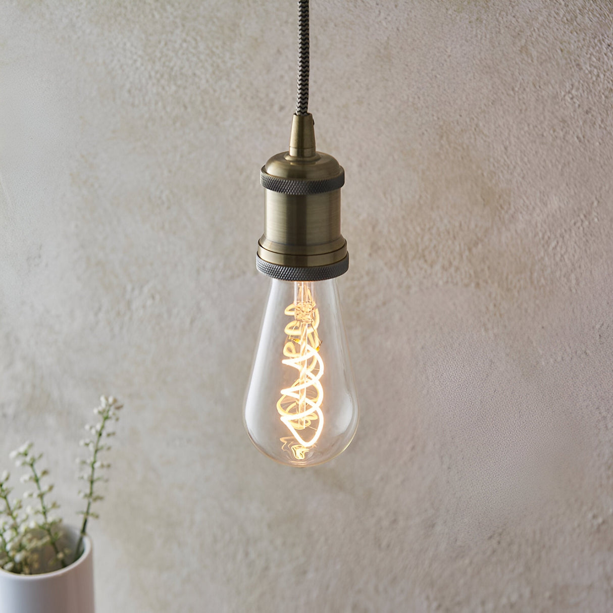 Endon 4W E27 LED filament twist bulb with clear pear-shaped glass and warm amber spiral filament, lit in an antique brass pendant holder against a pale wall.