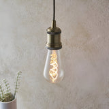 Endon 4W E27 LED filament twist bulb with clear pear-shaped glass and warm amber spiral filament, lit in an antique brass pendant holder against a pale wall.