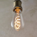 Endon 4W E27 LED filament twist bulb with clear pear-shaped glass and warm white spiral filament, fitted in an antique brass holder.