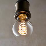 4W E27 LED filament GLS bulb with clear glass and spiral filament, warm white glow, fitted in a dark bronze pendant holder.