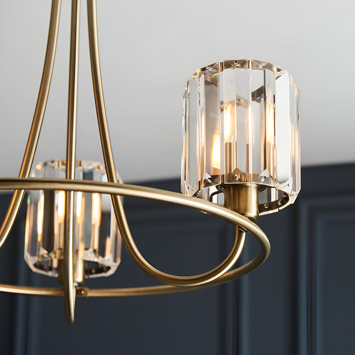 Close-up of Endon Clementine 3 light semi-flush ceiling light in brass with faceted glass shades, shown lit against a dark panelled wall.