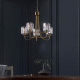 Endon Clementine 5 light pendant in brass with curved arms and cut faceted glass shades, hanging above a dining table against a dark panelled wall.