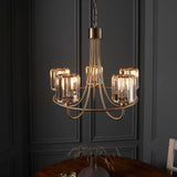 Endon Clementine 5 light pendant in brass with curved arms and clear cut faceted glass shades, hanging on a chain against a dark grey panelled wall.