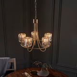 Endon Clementine 5 light brass pendant with cut faceted glass shades on curved arms, hanging from a chain above a wooden dining table.