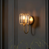 Endon Clementine wall light in brass with a cut faceted glass shade and curved arm, mounted on a grey panelled wall for ambient bedroom or hallway lighting.