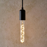 Endon 4W E27 LED filament bulb with clear tubular glass and warm white spiral filament, suspended from a matte black pendant holder against a beige wall.