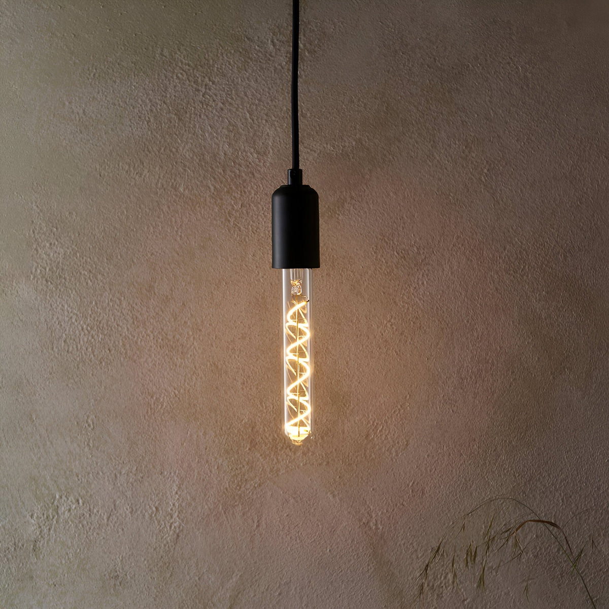Endon 4W E27 LED filament spiral bulb in a clear tubular glass, warm white glow, fitted in a matte black pendant holder against a textured beige wall.