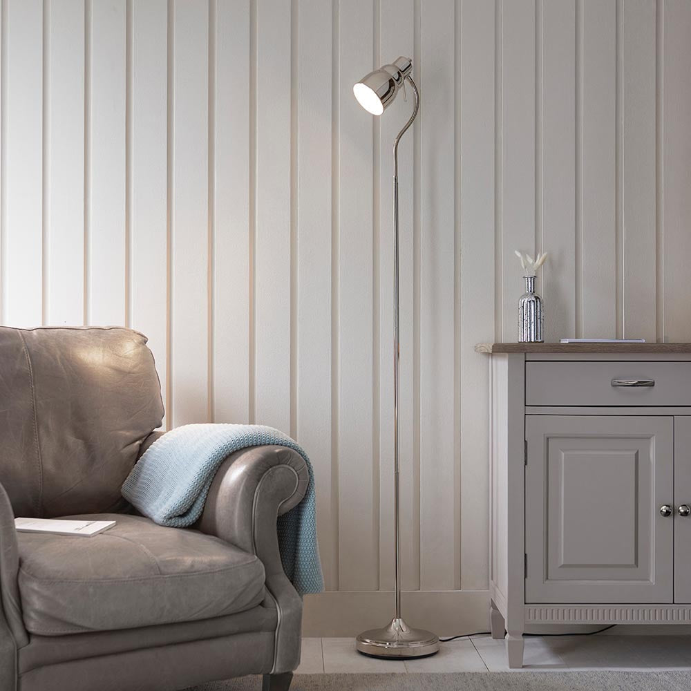 Endon Bevleigh nickel floor lamp with a flexible adjustable arm and round base, positioned beside a grey leather armchair and pale panelled wall.