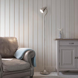 Endon Bevleigh nickel floor lamp with a flexible adjustable arm and round base, positioned beside a grey leather armchair and pale panelled wall.