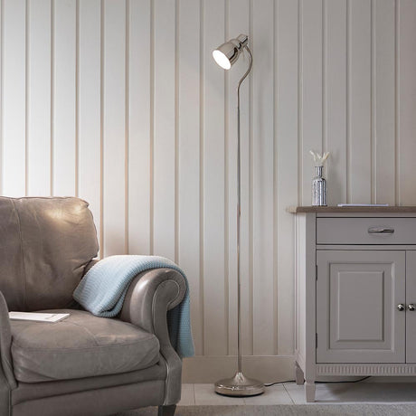 Endon Bevleigh nickel floor lamp with a flexible adjustable arm and round base, positioned beside a grey leather armchair and pale panelled wall.