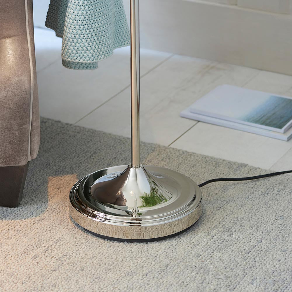Endon Bevleigh floor lamp base in polished nickel with slim stem, set on a light grey rug beside a leather chair and open magazine on tiled flooring.