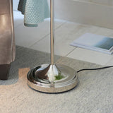 Endon Bevleigh floor lamp base in polished nickel with slim stem, set on a light grey rug beside a leather chair and open magazine on tiled flooring.