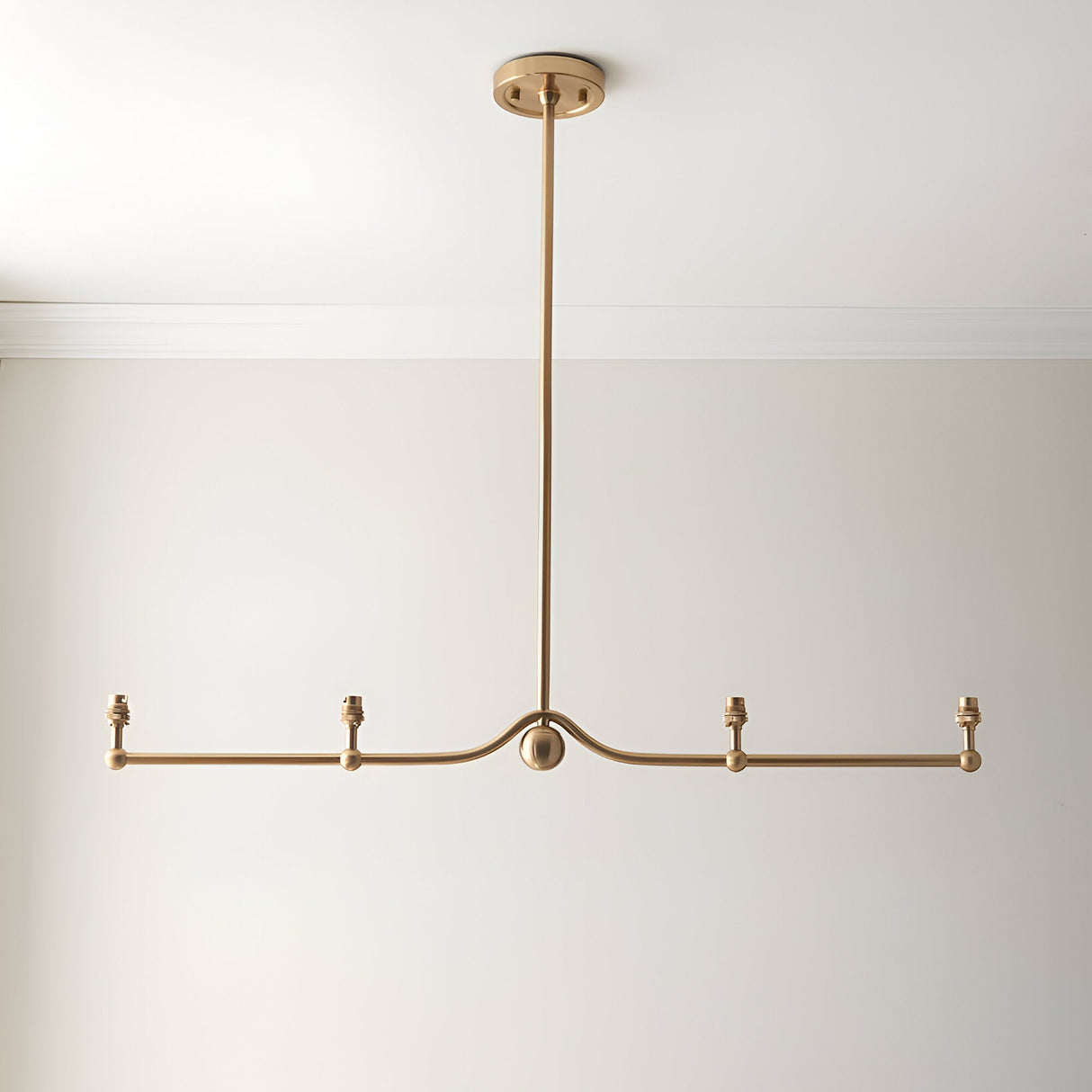 Endon Cliffleigh 4 light linear pendant in brushed aged brass, with a horizontal bar, sphere detail, B22 lamp holders and no shades, on a white ceiling.