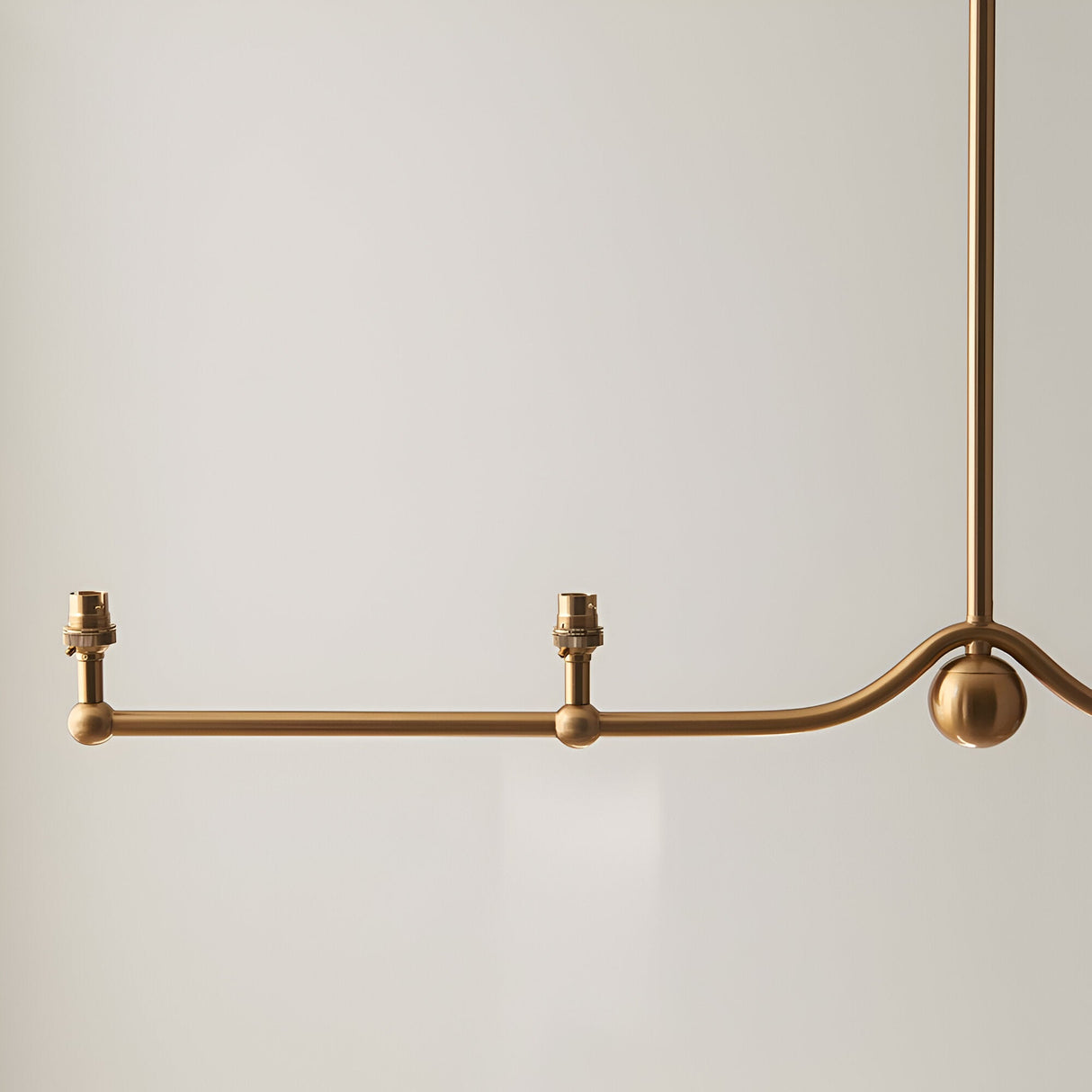 Endon Cliffleigh linear pendant detail in brushed aged brass, showing the curved bar with sphere accent, two visible B22 lamp holders, and drop stem.