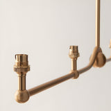 Close-up of Endon Cliffleigh 4 Light Linear Pendant in brushed aged brass, showing B22 lamp holders and decorative sphere detail along the bar.