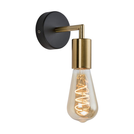 The SENA Wall Spotlight is a wall-mounted light fixture that boasts a matte black circular base and a brushed gold arm and socket. It features an exposed Edison bulb with a visible filament, casting a warm glow. This spotlight is the perfect match for the SENA pendants in any space.