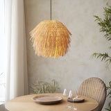 Chartleigh Pendant Shade in natural rattan with layered, spiky texture, lit above a wood dining table in a neutral-toned room.