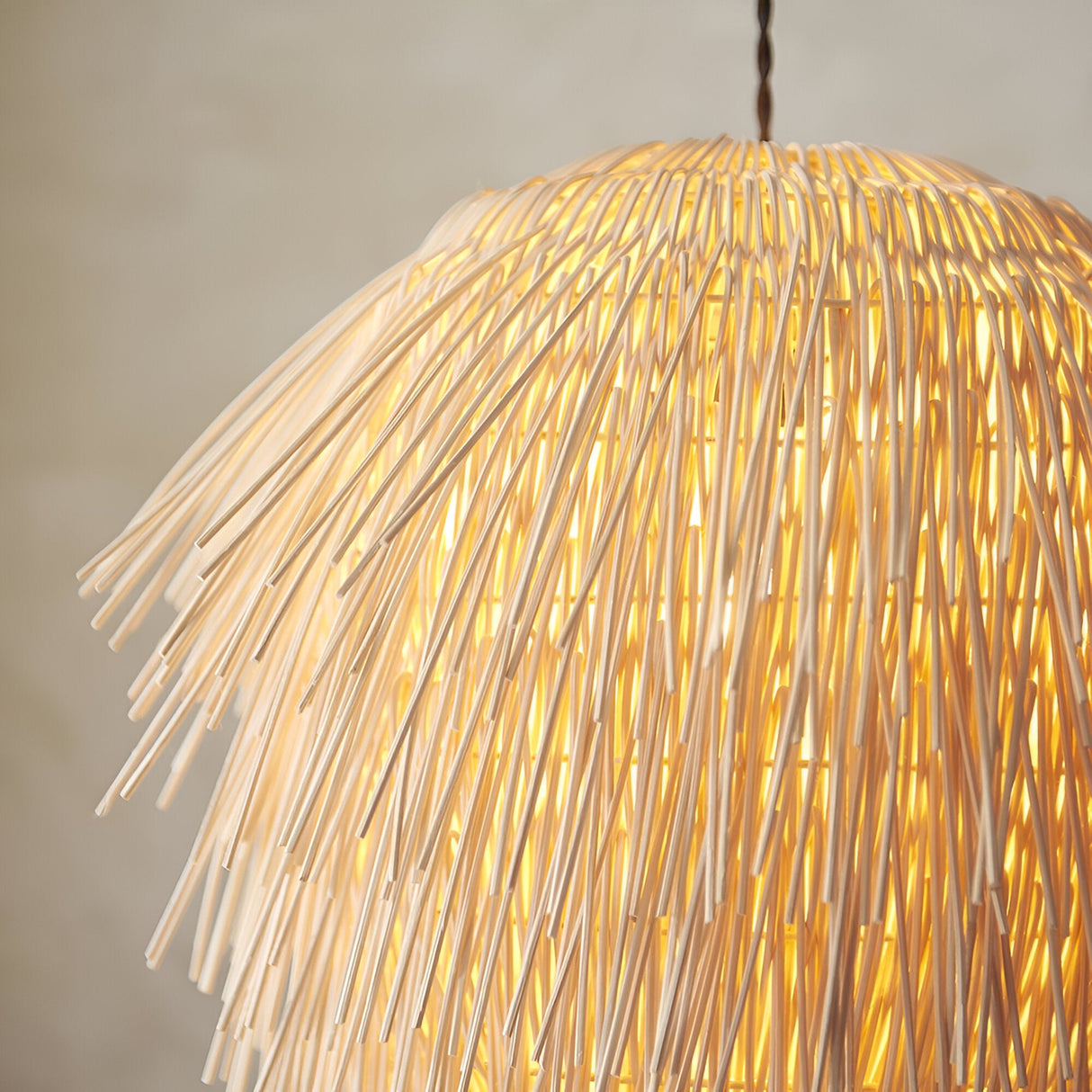 Chartleigh Pendant Shade in natural rattan, dome-shaped with overlapping fringed strands diffusing warm light, shown lit against a plain background.