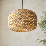 Endon Cranley pendant shade in natural handwoven rattan with a rounded drum shape, illuminated to show its open weave against a pale wall.