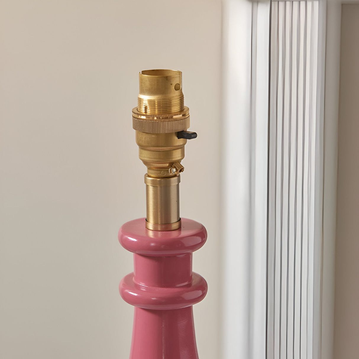 Close-up of the Endon Carlworth table lamp's brass B22 switched holder atop the pink gloss resin turned spindle base, beside a bright window.