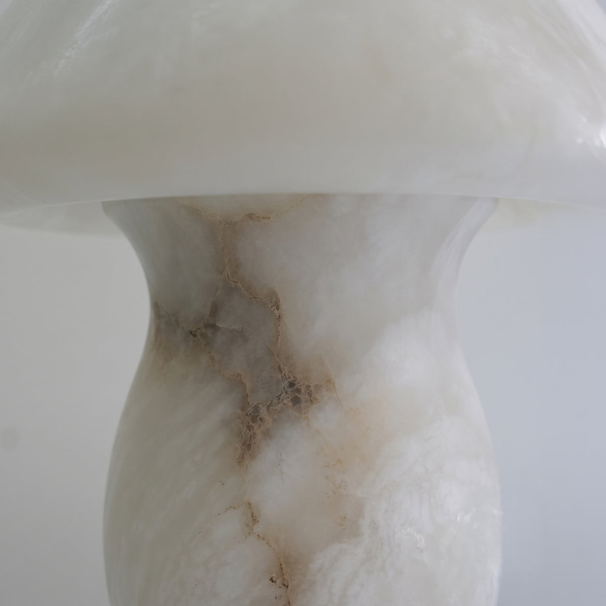 Close-up of the Morfia mushroom-form table lamp in solid alabaster, showing natural veining across the dome and stem on a plain white background.