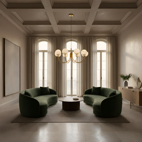 A modern living room with two curved green sofas, a round coffee table, arched windows with white curtains, neutral walls, a sideboard with decor, and the Aurelio 8 Light Large Globe Alabaster Chandelier in Soft White & Brushed Brass overhead.