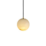 Niori Lyvane Extra Small Alabaster Globe Pendant Light in brushed brass with spherical Spanish alabaster shade on black cable, lit on white background.