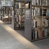 Sisal A/01 LED outdoor wall light in brown, with woven fibre front panel and square frame, shown mounted above bookshelves in a library setting.