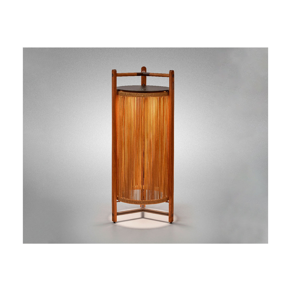 Kando P/111/R rechargeable outdoor floor lamp with sand nautical cord cylinder in a teak wood frame, three-legged base, and brown top disc, glowing warmly on a plain grey background.